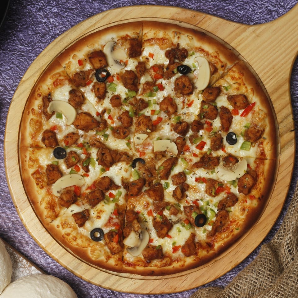 Guido's Pizza & Pasta's chicken pizza with mushrooms, olives, and bell peppers on a wooden board.