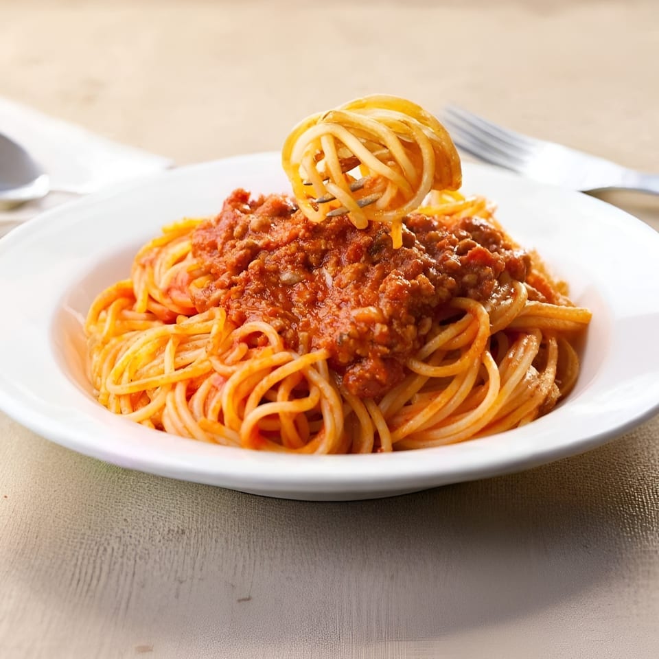 Spaghetti Bolognese with a fork twirling pasta, served in a white bowl on a light wooden table.