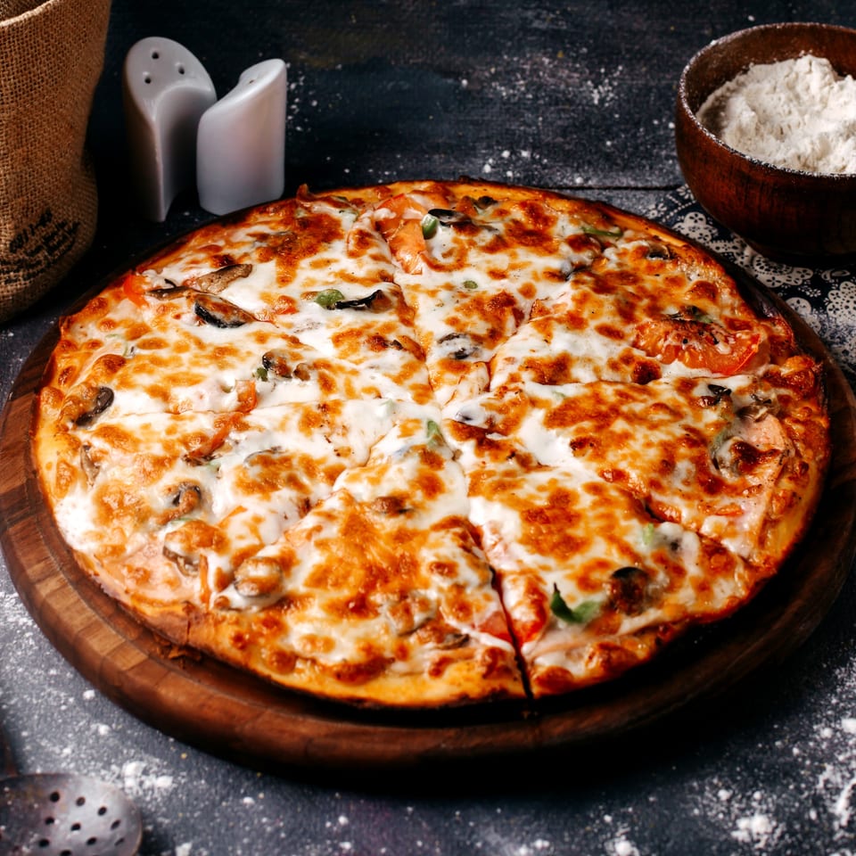A freshly baked, sliced Guido's Pizza with melted cheese and toppings on a wooden board.
