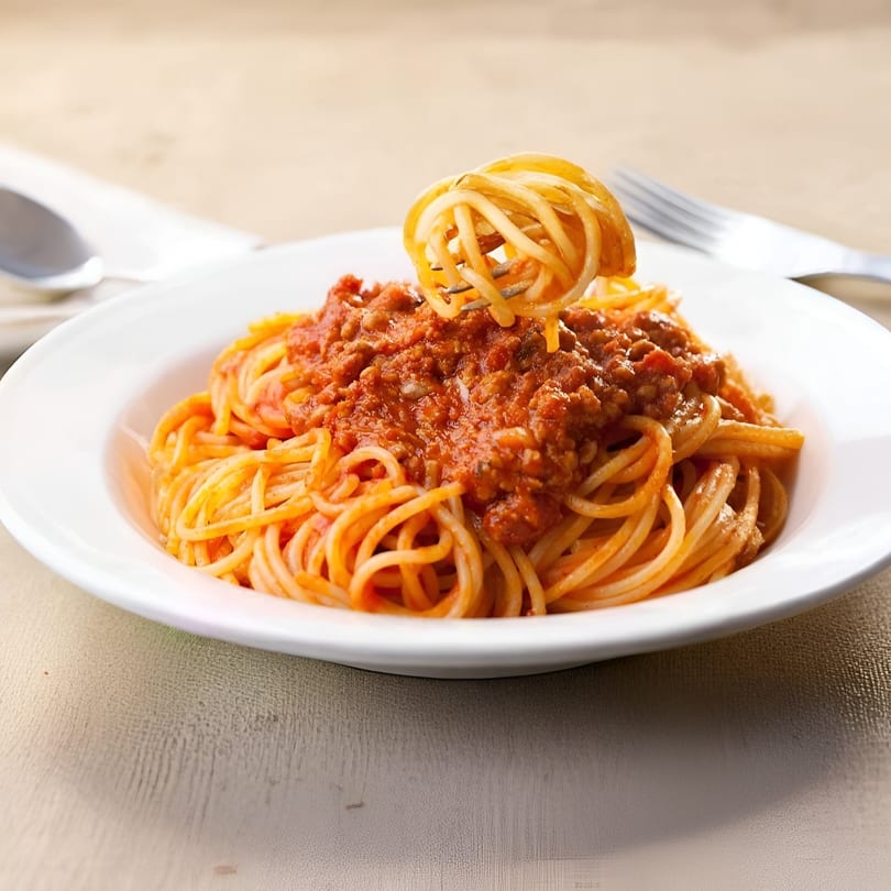 A fork twirls spaghetti with rich Bolognese sauce from a white plate at Guido's Pizza & Pasta.